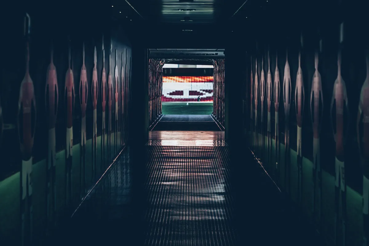 Soccer stadium with red seats and a lit pitch seen from the players tunnel